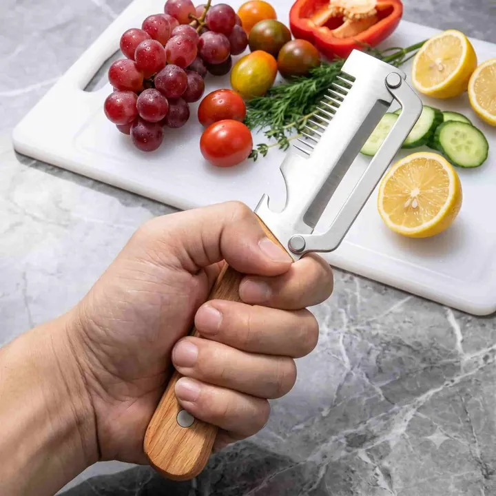 Hand met de PeelPro-dunschiller boven een snijplank met tomaten, druiven en een citroen